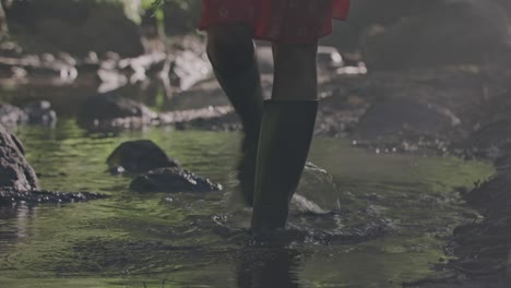 Enchanted-Forest-Stroll:-Close-up-of-a-woman's-boots-as-she-is-walking-through-a-pool-of-water-in-a-fairy-tale-like-lush-forest-amid-the-mystical-morning-mist-and-fog