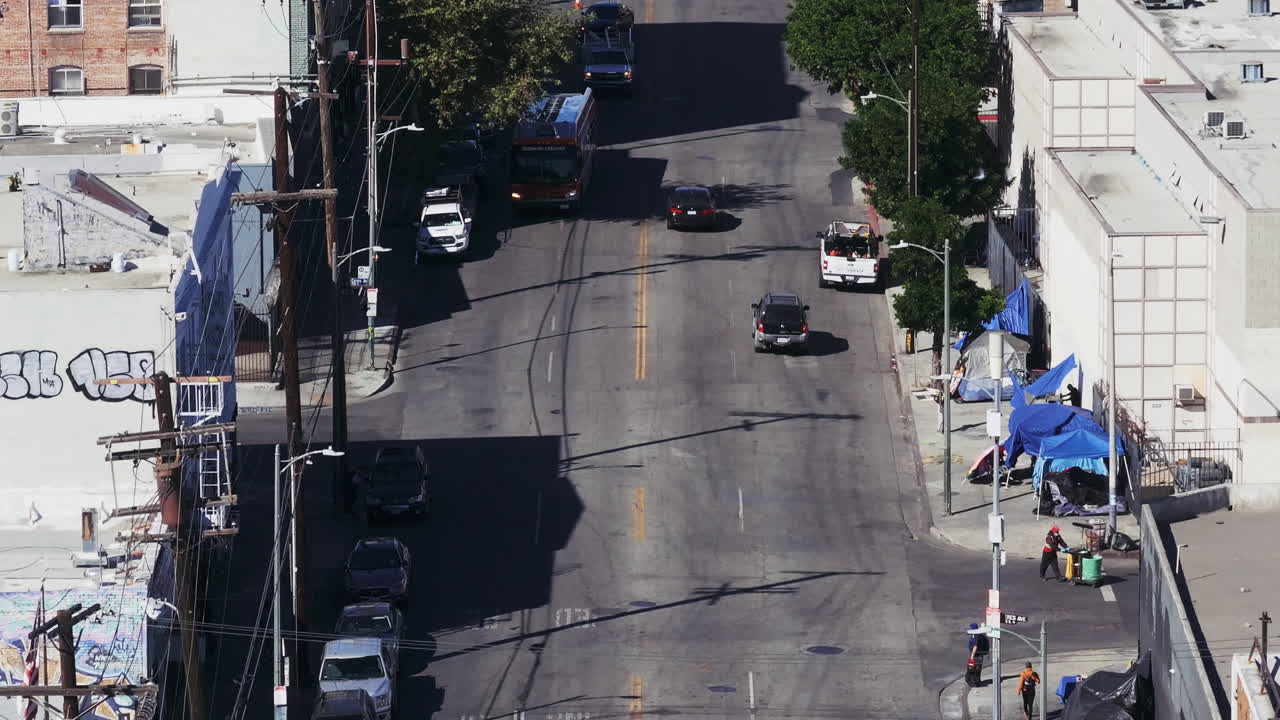 High-angle view of a city street with traffic, buildings, and a roadside encampment