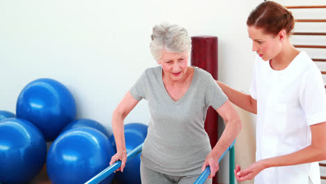 Lächelnder-Physiotherapeut-Hilft-Patienten-Beim-Gehen-Mit-Barren