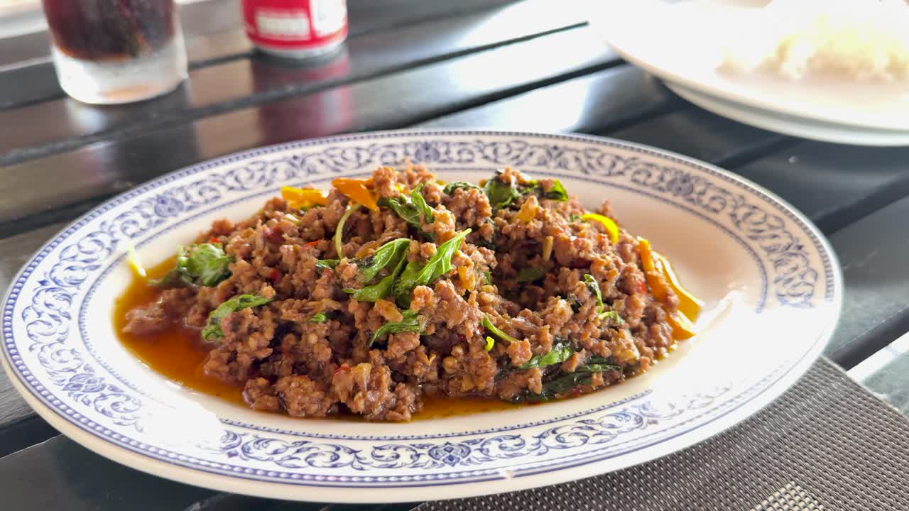 A vibrant minced chicken dish garnished with herbs, captured in natural light on a dining table in Phuket