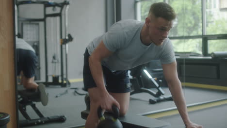 man doing kettlebell bench rows in gym
