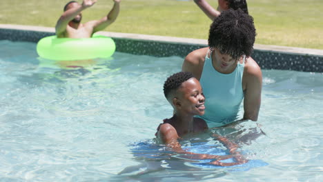 Madre-Afroamericana-Enseñando-A-Su-Hijo-A-Nadar-Con-Flotador-En-Una-Piscina-Soleada,-Cámara-Lenta