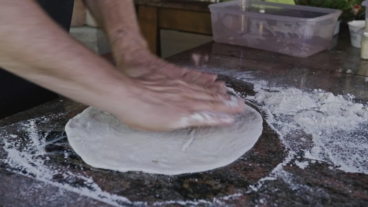 Chef che stende l'impasto della pizza con le mani in una cucina rustica all'aperto