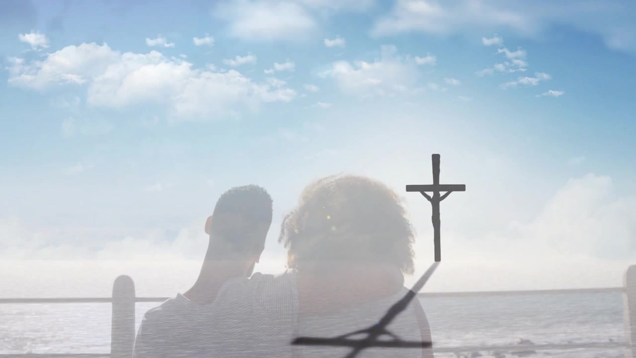 Casal se abraçando enquanto olha para uma cruz com vista para o oceano