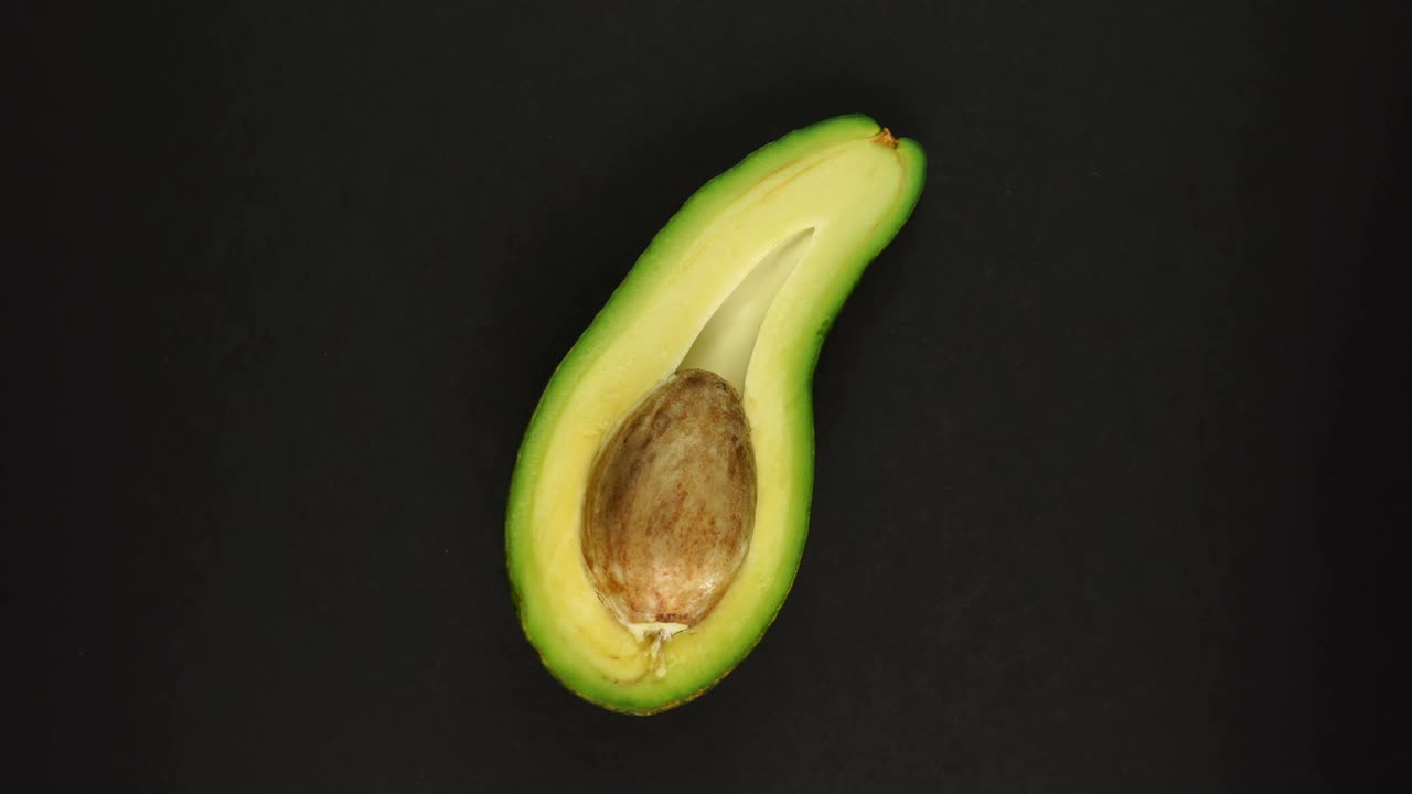 Avocado tagliato maturo e biologico che ruota velocemente su sfondo nero