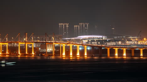 illuminated bridge at night with city skyline and motion-blurred boat