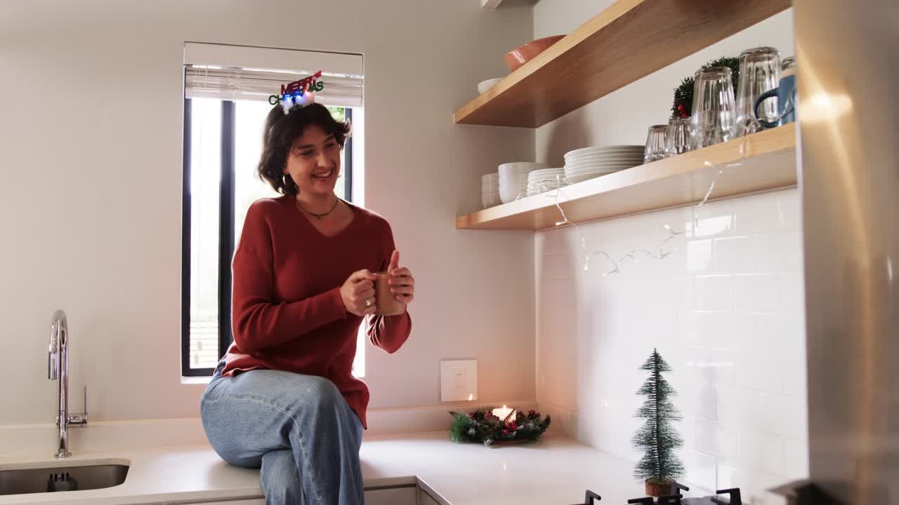 Dopo aver notato un'esposizione festiva sullo scaffale, donna con una fascia per capelli che sorseggia da una tazza sul bancone della cucina