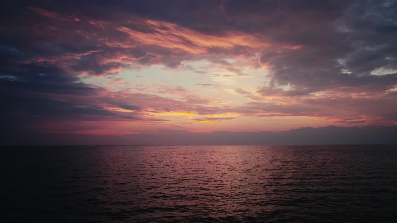 Vivid sunset over tranquil ocean, clouds streaking the sky with purple and orange hues, reflecting on water
