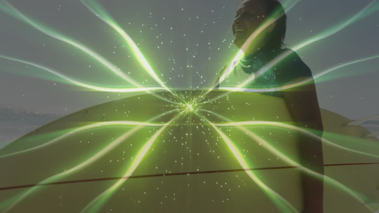 Senior woman standing at beach edge, holding yellow surfboard, showing glowing green health energy