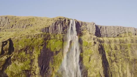 Large-Iceland-waterfall-cascading-over-highland-cliff,-aerial-forward-reveal