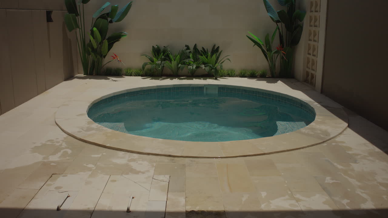 Minipiscina rotonda in un cortile tropicale privato con acqua cristallina, pavimentazione in pietra e piante lussureggianti che creano un tranquillo rifugio in villa.
