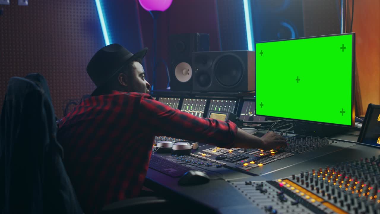 Elegante ingegnere del suono / produttore che lavora in uno studio di registrazione musicale, usa un computer con schermo verde, mixer ed equalizzatore per creare un nuovo brano di successo. Artista musicista nero creativo. Ritratto di profilo