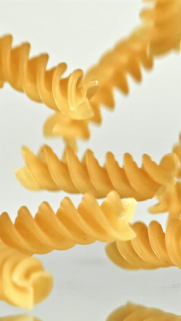 Slow Motion of Uncooked Fusilli Pasta Falling on a White Background