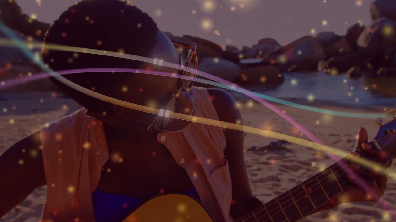 Woman glancing over shades, strumming guitar on shore, light streaks sweeping frame enhancing music