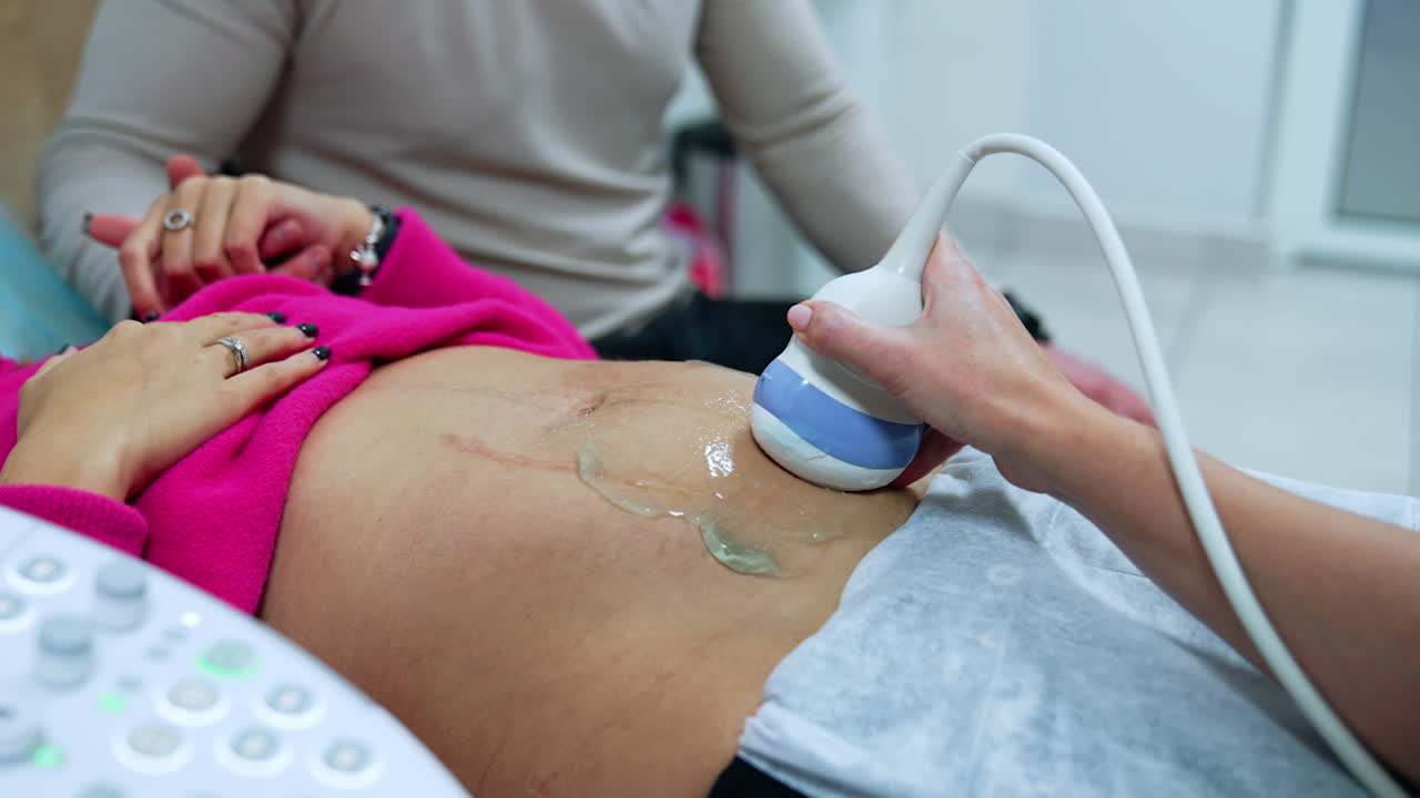 Doctor's hand moving the device by the belly of a woman. Ultrasound check up of pregnancy.