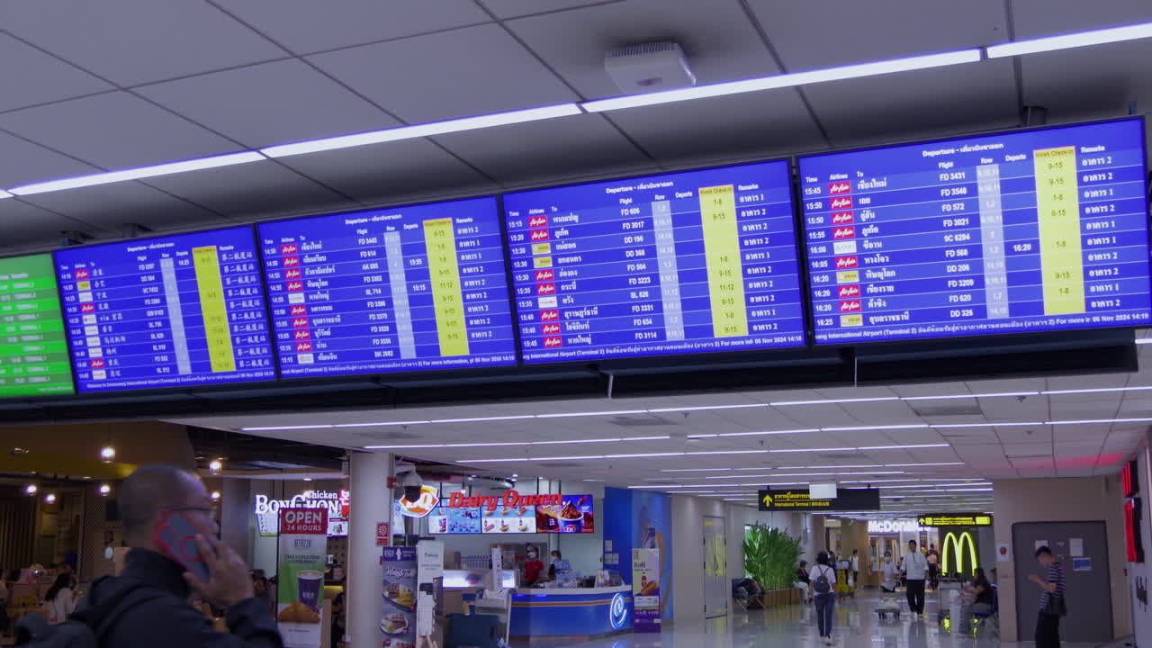 A flight display screen at Don Mueang Airport shows current flight schedules for travelers. Great for air travel and airport themes.