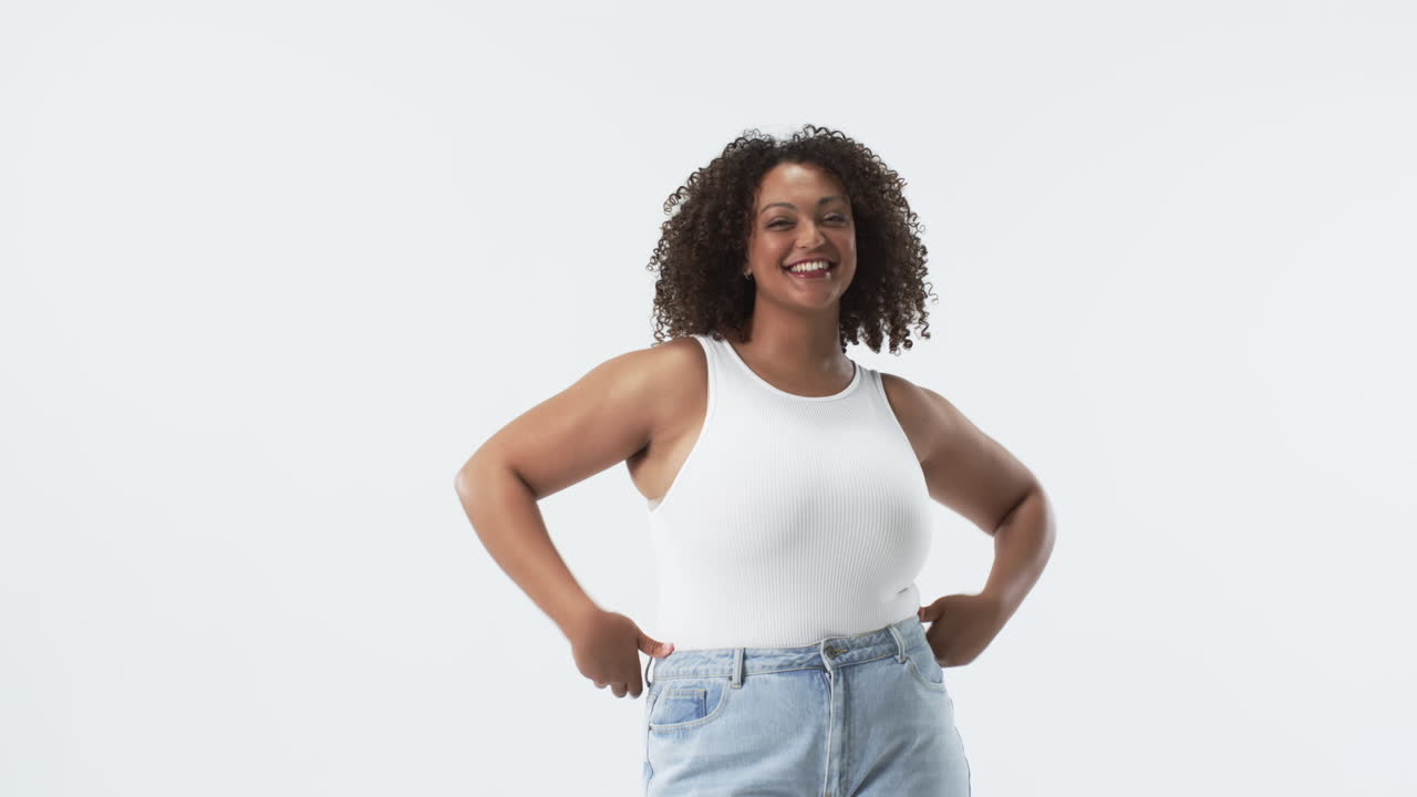 Young biracial plus size woman with curly hair smiling and posing in studio