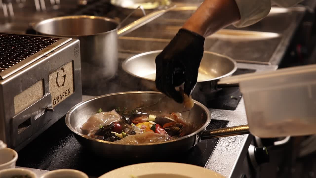 Chef's Hand Adding Ingredients to a Frying Pan in a Professional Kitchen
