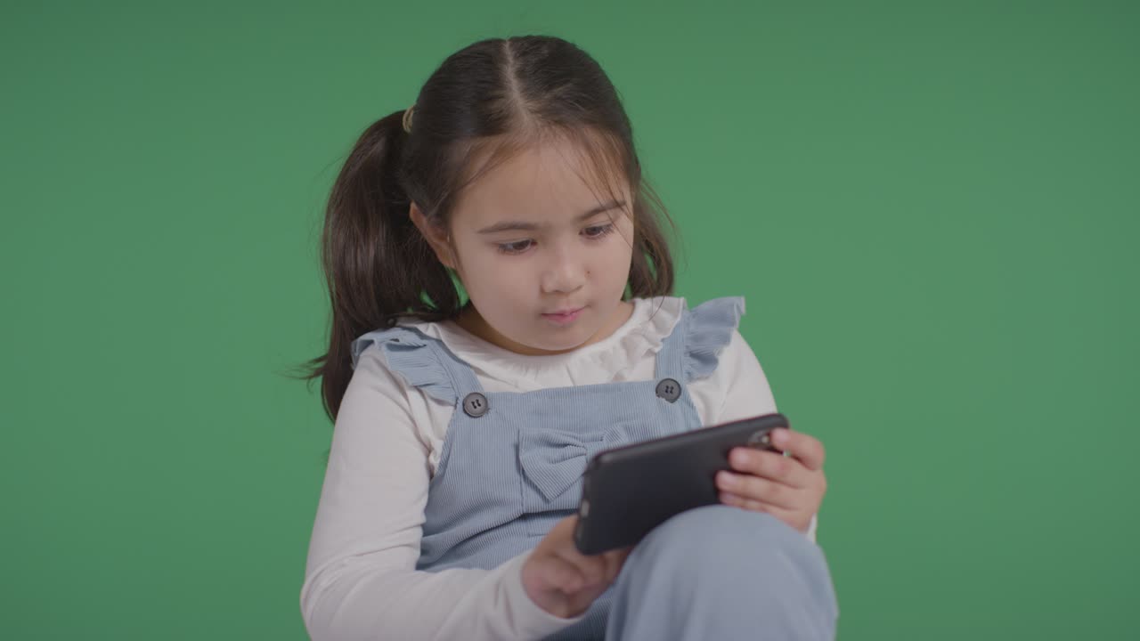 Studio Portrait Of Young Girl On ASD Spectrum Playing With Mobile Phone On Green Background 3
