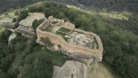 sunlight illuminates the eighth century taradell castle, perched atop a large rock formation, surrounded by lush greenery in the catalonian landscape
