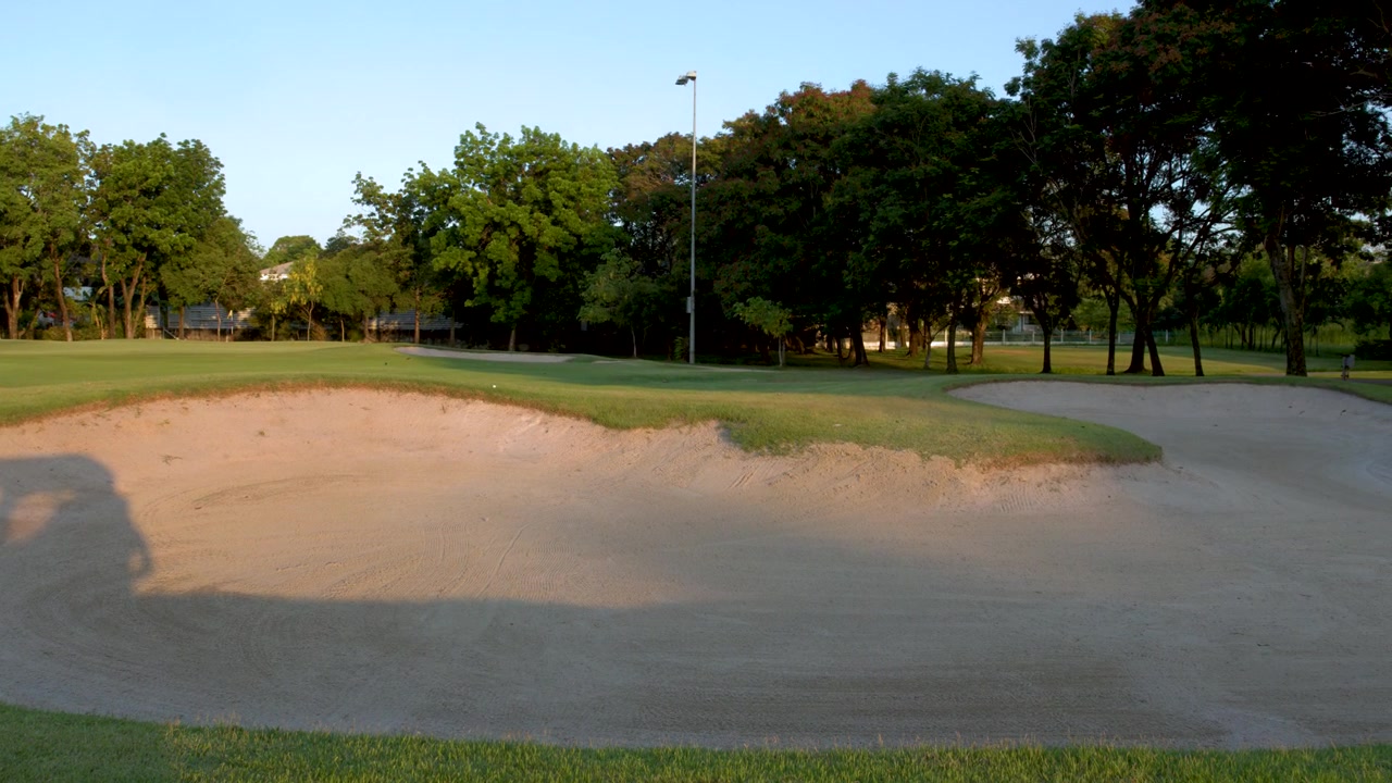 Inquadratura ampia di un bunker di un campo da golf con l'ombra di un carrello che si muove sotto il sole splendente