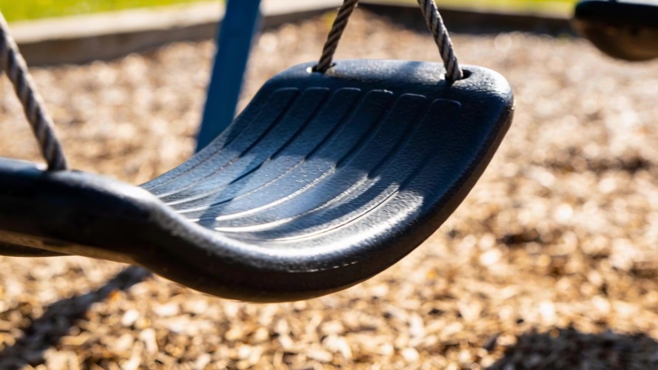 Seggiolino dell'altalena in plastica nera modellata che oscilla per la leggera brezza al parco giochi, con corde attorcigliate