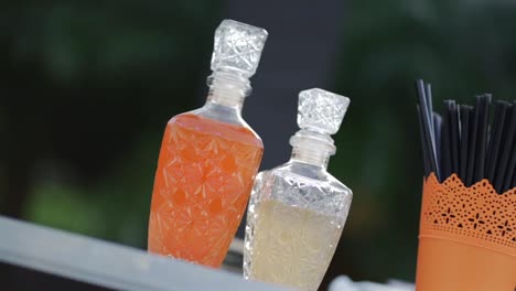 Two-liquor-decanter-bottles-and-container-with-straws-on-bar-counter-at-summer-party