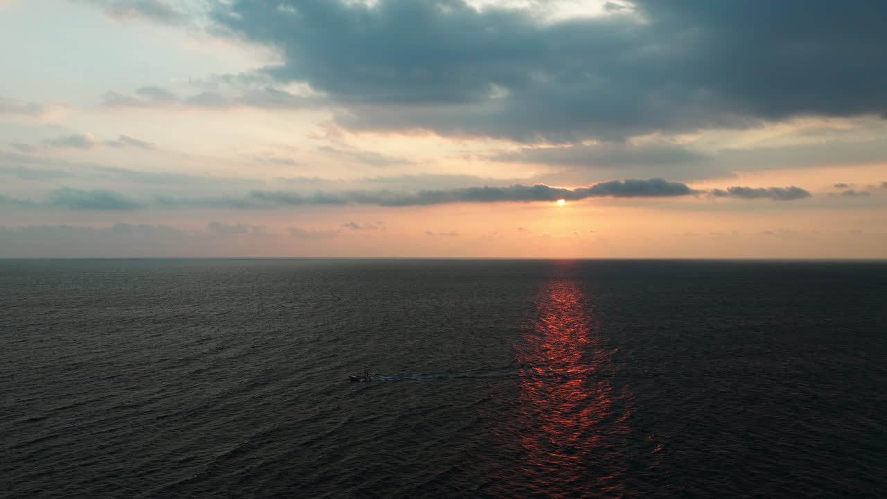A fishing boat sails through shimmering waters at sunset, casting long shadows over the Indian Ocean. A peaceful aerial view of Sri Lanka's coastal charm, golden light, and calm sea