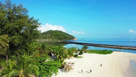 Tourists-enjoying-white-sandy-beach-and-beautiful-resort-park-with-palm-trees-in-front-of-blue-sea-on-tropical-island-in-Thailand