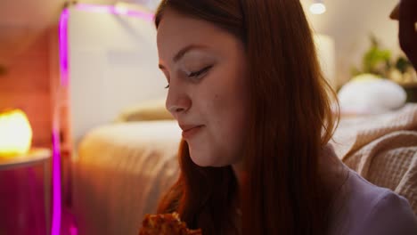 una adolescente comiendo pizza en el dormitorio.