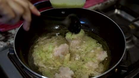 Close-up-of-hand-stirring-frozen-onions-and-spices-in-a-skillet-on-a-stove