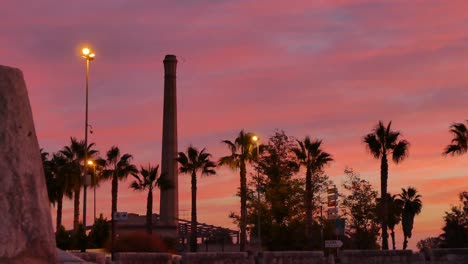 Schöner-Zeitraffer-Eines-Sonnenaufgangs-Mit-Vorbeifahrenden-Autos-Und-Im-Hintergrund-Der-Turm-Einer-Alten-Fabrik