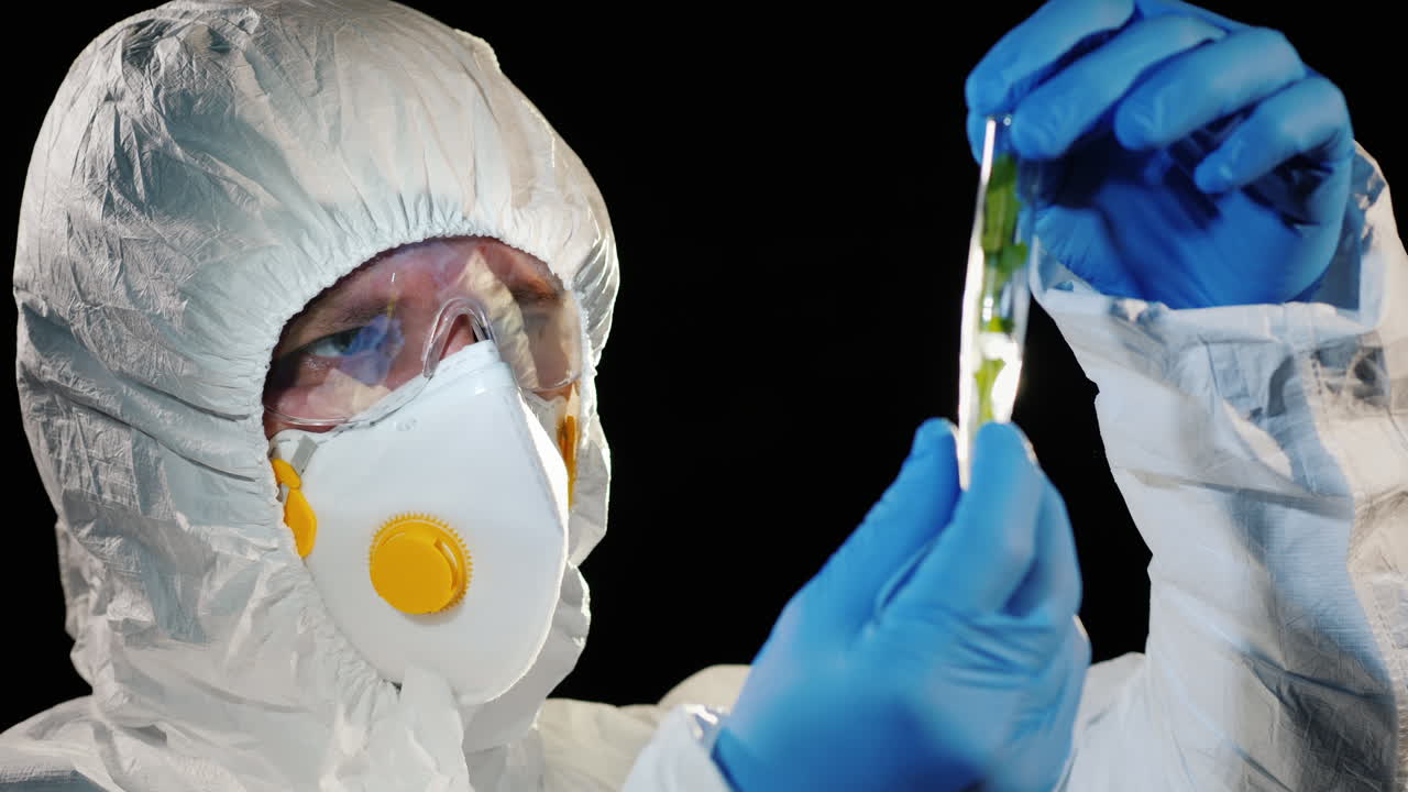 보호복을 입은 연구원이 식물 샘플이 있는 시험관을 보고 있다