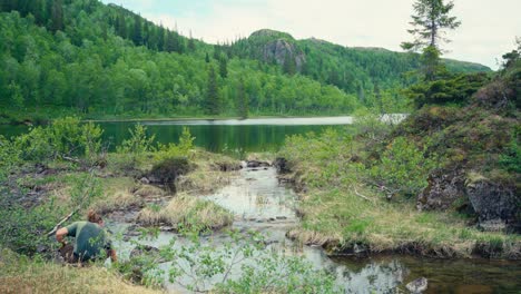 un hombre está llenando su vaso con agua del lago entre imefjelsvatnet y gurben, indre fosen, trøndelag, noruega - toma estática