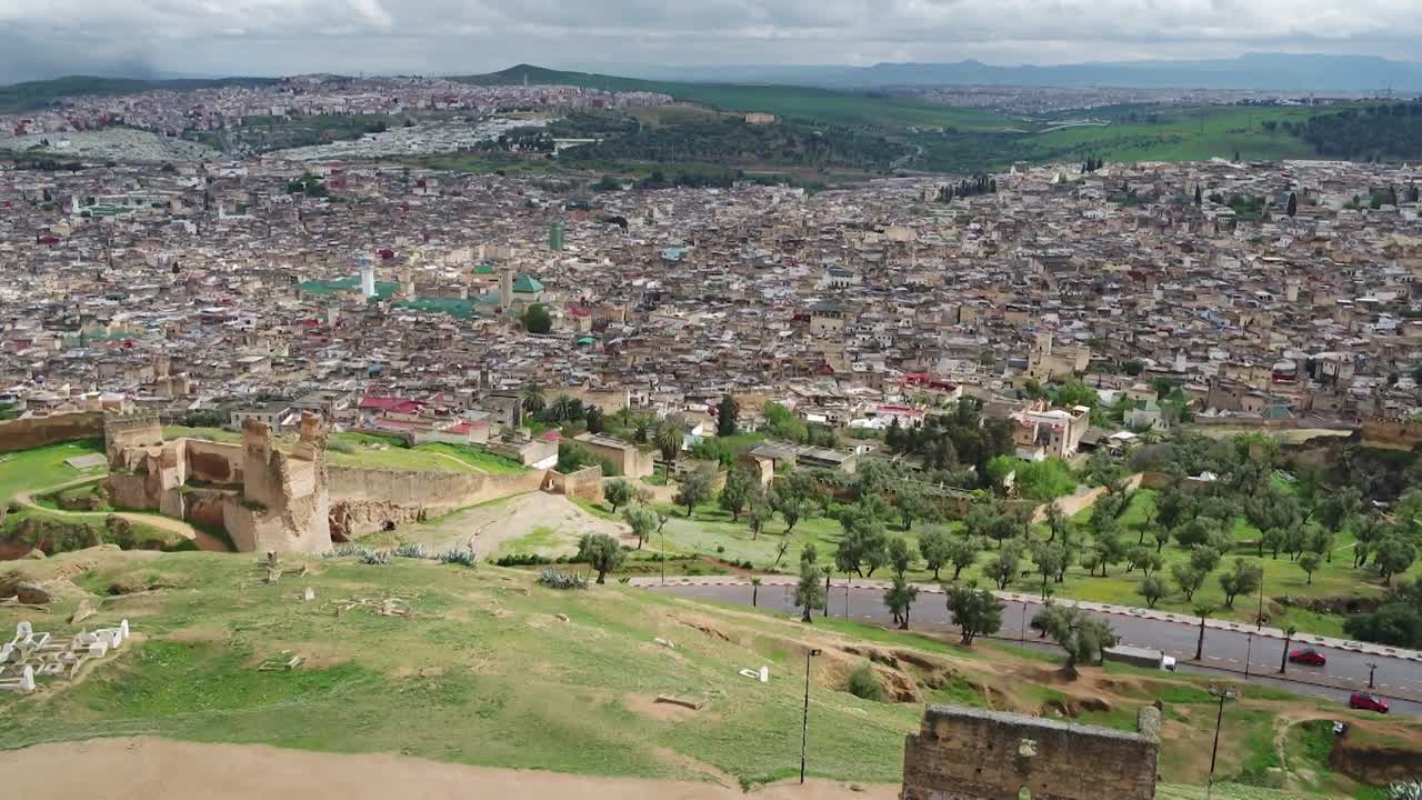 Maestosa ripresa con drone delle Tombe Merinidi del XIV secolo. Mostra le rovine storiche sulla cima della collina con un'ampia vista panoramica sulla fitta Medina di Fez e sulle circostanti montagne dell'Atlante
