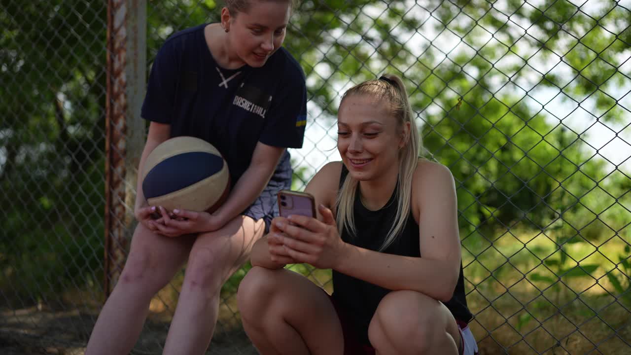 두 명의 여성이 농구장에서 전화를 보고 있습니다.