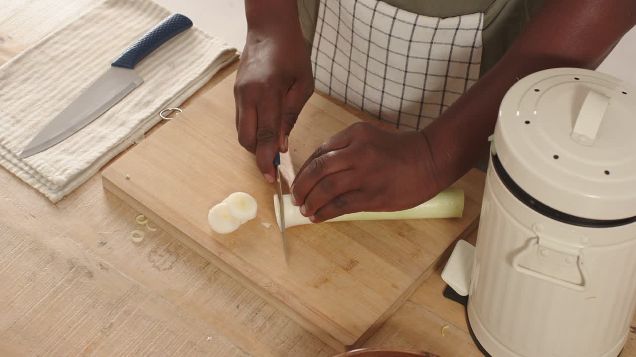 Chef's knife is slicing white-and-light-green leek into thin rounds on wooden cutting board
