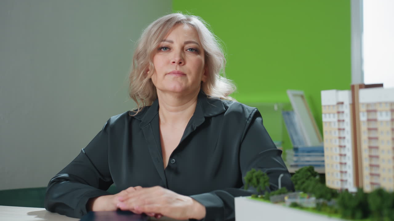 real estate professional closes book and gently drops pen on cover beside detailed architectural model, seated at modern desk in brightly lit office environment with organized background