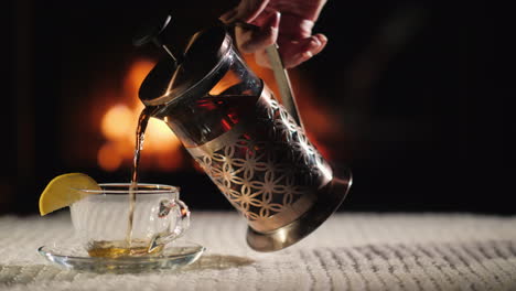 Pour-Tea-Into-A-Cup-On-The-Background-Of-The-Fireplace-Tea-In-A-Cozy-Setting