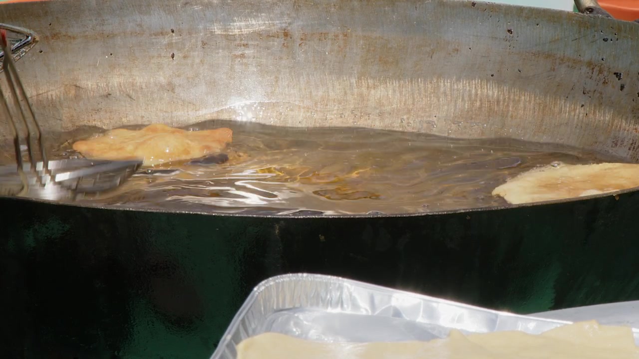 Poori puff bread fries in vat of oil at outdoor Indian food festival