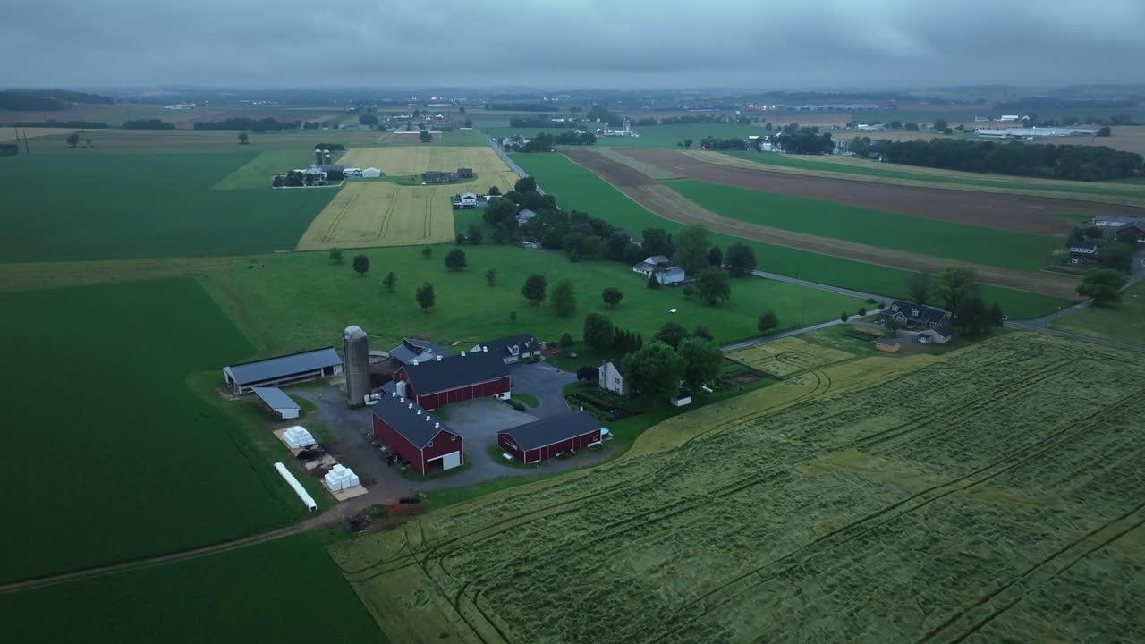 Harvested and cut fields in countryside of America. Drone flyover shot. Dark morning in USA. Red barns and silo storage on farmstead. Kansas, America. Cloudy day in summer