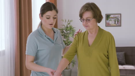 elder woman holding a dumbbell raising an arm up assisted by a female doctor 2