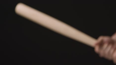 close up of player swinging wooden baseball bat at ball against black studio background