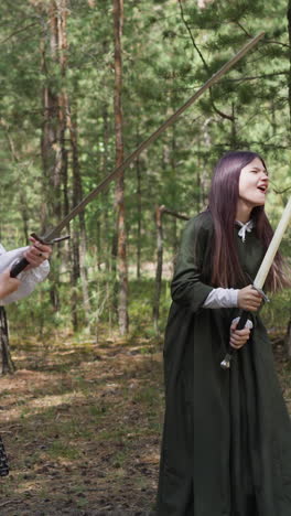 role-player girls in vintage apparel fight on swords in sunny pine wood slow motion. historical armour in modern life. reconstruction activity and leisure