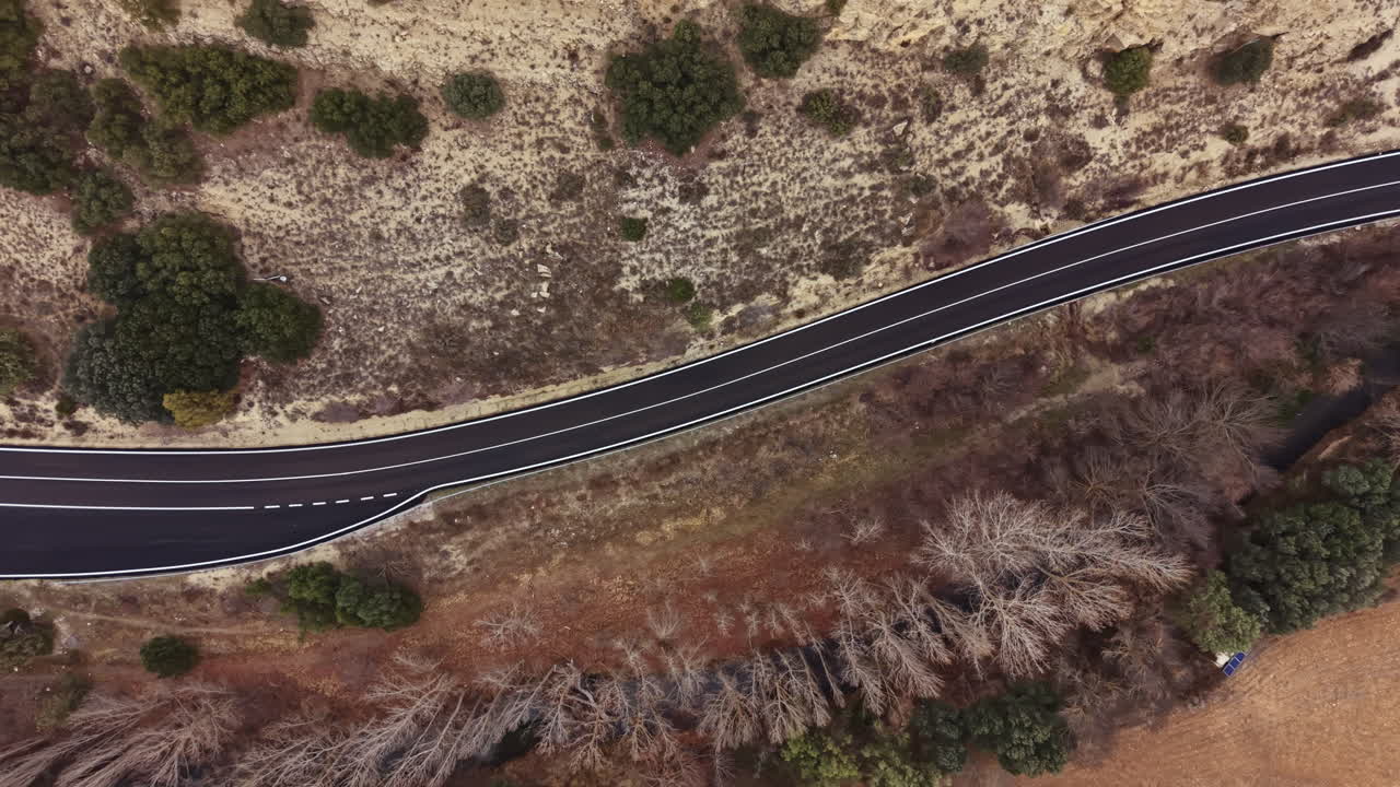 Route sinueuse entourée de terres arides et d'arbres en milieu rural sous un ciel dégagé en plein jour