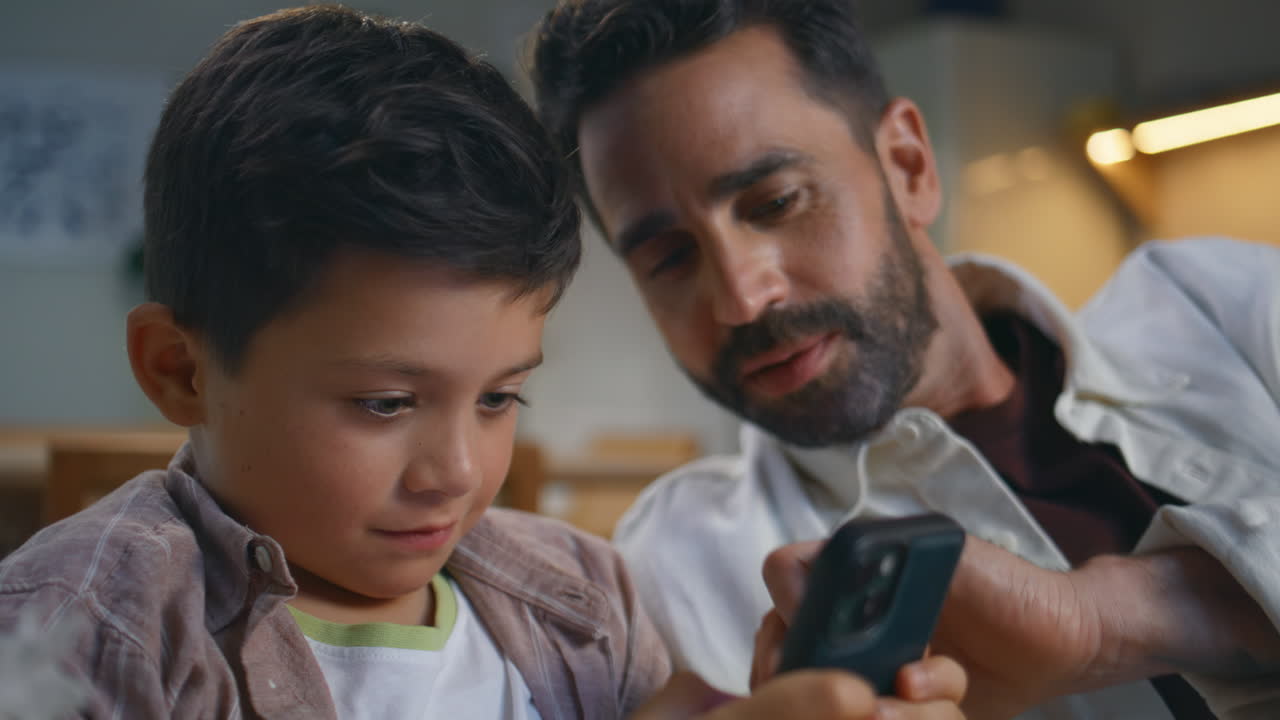 Father son playing cellphone game at evening home closeup. Man kid inonline
