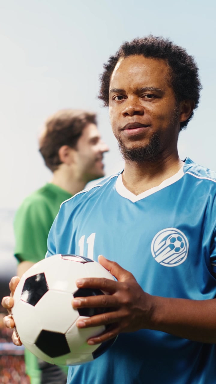 Video verticale: ritratto di un calciatore afroamericano che posa con il pallone sul campo.