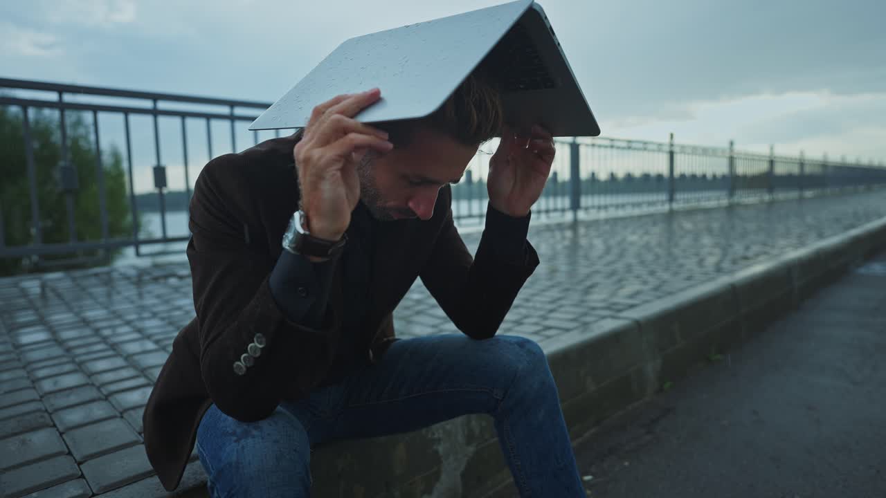 Man sitting on the street with a laptop during a rainy day