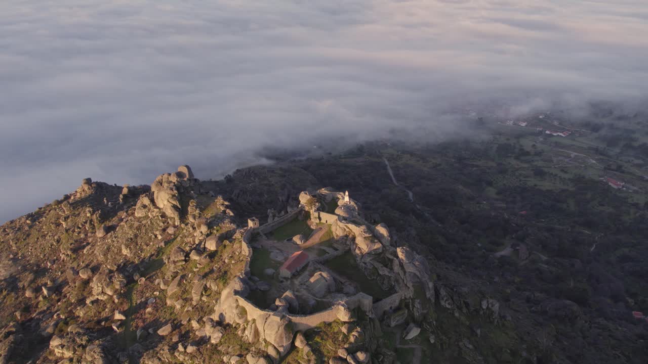 Tilt up shot of old Ru&iuml;ne Castelo de Monsanto on mountain top with low clouds in the morning, aerial