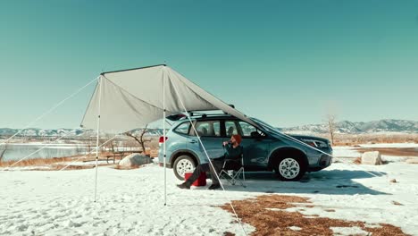 un hombre milenario con vista a un hermoso lago de invierno debajo de un toldo para acampar